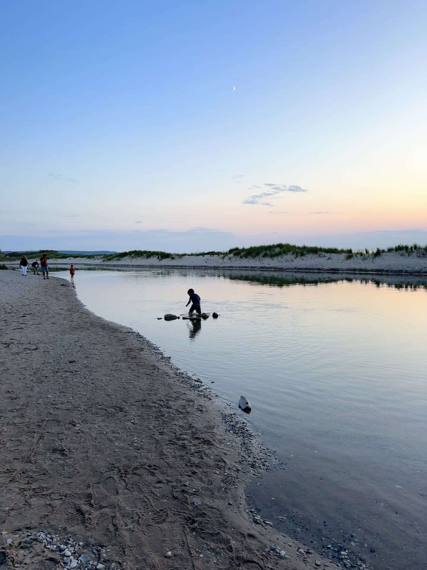Family at the Platte River mouth at dusk, a child stepping across stones