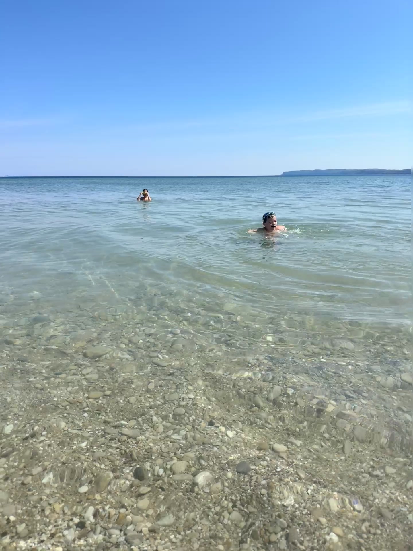 Kids swimming in the clear water of Lake Michigan with the Manitou Islands on the horizon