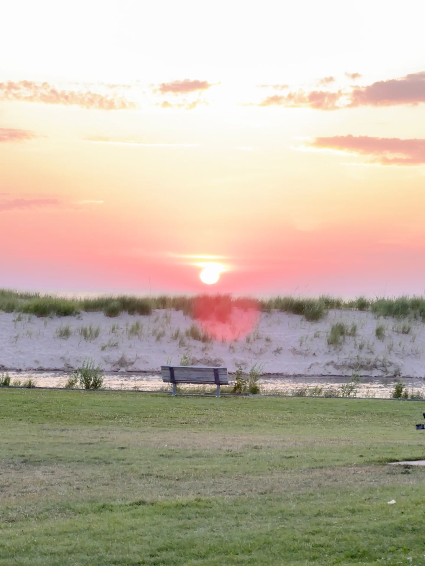 A bench overlooking the beach dunes at soft pink and orange sunset